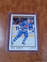 Front view of Joe Sakic O-Pee-Chee 1991-92 hockey card in blue Quebec Nordiques uniform, housed in protective plastic case.