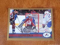 Front view of oversized hockey card showing Patrick Roy in Colorado Avalanche goalie gear actively defending net during a game. Card has gold border, O-Pee-Chee logo top right. Close-up detail of the card condition.