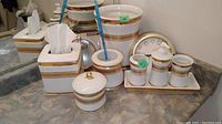 Full view of Hawthorne bathroom accessories including tissue cover, soap dispenser, containers, cups on tray, garbage can, toilet brush holder, and wall clock on a countertop.