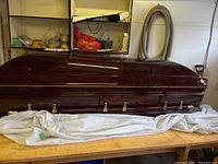 Closed casket side view showing glossy mahogany exterior and six gold-tone handles.