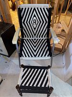 Front view of metal lawn chair with new black and white woven webbing, featuring the letter R in the pattern, and the wooden footstool with matching webbing in front