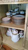 Top shelf with cups and plates showing white porcelain with gold trim and decorative designs.