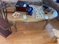 Full view of light tan wood coffee table with curved carved legs and decorative apron, holding various items on top.