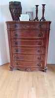 Front view of dark brown carved wooden dresser with six drawers and items on top