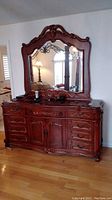Full front view of wood dresser with attached mirror, showcasing the overall design, carved details, and polished stone top.