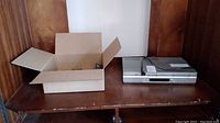 Open cardboard box containing multiple remote controls next to the Sony player.