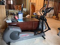 Side view of Life Fitness 9500HR elliptical in basement with surrounding furniture and items.