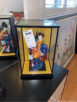 Front view of the doll inside the glass display case showcasing the colorful kimono and gold hairpiece
