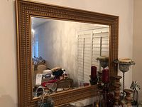 Front view of large rectangular mirror with wide decorative gold frame showing carved details and mirror surface reflecting room.