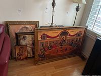 Four religious framed pictures leaning against wall including a large Last Supper painting and three smaller religious portraits.