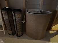 Photo of three rugs rolled up and standing, two with traditional patterns and one plain beige runner.