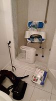 White bath seat with blue backrest, suction feet, reacher tool and humidifier in shower curb