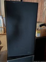 Front view of one black Acoustic Audio floor standing speaker showing the speaker cloth covering