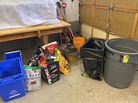 Overall photo of bins, bags of soil and grass seed, Ridgid shop vac, orange bucket in garage setting