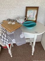 Full view of kidney-shaped white table displaying all items including towel, cutting board, salt and pepper shakers, teapot, serving dish, and framed picture