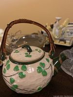 Front angle view of Japanese clover leaf ceramic teapot with bamboo handle, showing lid and surrounding items on table.