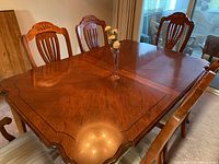 Solid wooden dining table with glossy finish and scalloped edges, six matching carved chairs around it
