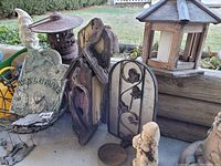 Outdoor setting photo showing entire assortment of garden items including wooden lantern, several cast iron plaques, carved wooden pieces, and garden statue.
