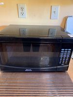 Front view of small compact black microwave showing Appliance Wholesale brand and digital keypad on right side.