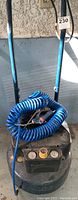 Full view of the black pancake air compressor showing blue coiled hose and handle.