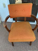 Front view of vintage orange upholstered chair showing wooden armrests and faded seat cushion