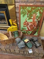 Photo showing all items in the lot including cars, cross stitch, squirrel resin figure, dust pan, crate, mug, and baskets arranged on a brick surface and hearth.