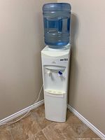 Full view of the Garrison water cooler with blue water jug on top, white body, and dual taps for water dispensing.