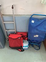 Photo showing two red Coleman cooler bags, silver 3 step ladder, and blue Canadian Camper backpack