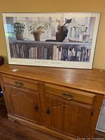 Wooden cabinet shown with framed art on top, showcasing the upper surface and overall cabinet design with drawers and cupboard doors.