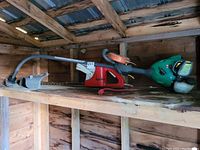 Twist and Edge gas-powered trimmer with green body and red cutting guard placed on wooden shelf