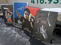 Four vintage horror movie posters leaning together outdoors on pavement, partially on snow and ice, showing titles The Evil Dead (two different posters), The Lost Boys, and Freddy vs. Jason