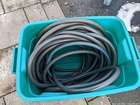 Photo of a 75 ft gray garden hose coiled inside a turquoise plastic bin outdoors on concrete and grass near snow patches.