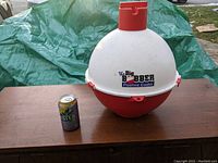 Photo of the Big Bobber floating cooler on a wooden surface next to a can for size comparison showing cooler shape and branding.