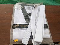 Newly packaged white Karate/MMA Gi with white belt, size medium, from Best Martial Arts brand in clear plastic packaging on wooden surface.