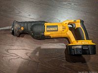DeWalt DC385 reciprocating saw with attached battery shown on floor, visible wear and dirt on tool body and rubber grip handle, blade attached on front.