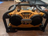Front view of DeWalt jobsite radio showing dual speakers, digital display, control buttons, and protective frame.