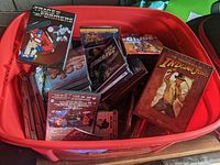 Top view of large red storage bin filled with more than 50 DVDs and DVD sets including Transformers, Indiana Jones, G.I. Joe, and others.