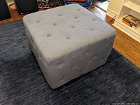 Square grey fabric ottoman showing tufting and fabric texture