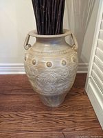 Close-up of ceramic vase showing textured finish, raised circular and swirling patterns, and handles