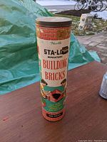 Photo of vintage Sta-Log cylindrical container with colorful label and text describing the miniature building bricks toy set from the 1950s.