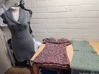 Three women's knit dresses and tops on table and mannequin, showing various colors and knit styles.