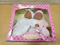 Front view of boxed baby dolls set with one doll in white sleeper and one in pink sleeper