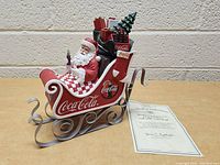 Side view of the Coca-Cola Santa Claus figurine and Certificate of Authenticity on a wooden surface against a brick wall.