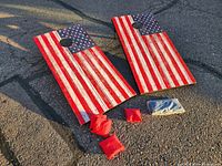 Pair of cornhole boards laid flat on pavement, showing American flag painted design and bean bags in front.