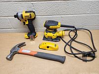 DeWalt drill, palm sander, Zircon stud finder, and HDX hammer on table against cinderblock wall.