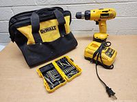 Image showing one DeWalt cordless drill upright with battery attached, charger, bit set open, and DeWalt branded soft carrying bag behind.