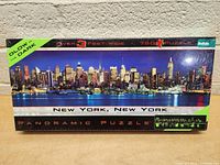 Front view of the box showing New York city skyline puzzle image, glow in the dark label, puzzle size and piece count