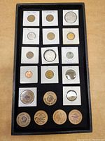 Photo of assorted tokens mounted in white cardboard holders and wooden nickels arranged in a black tray.