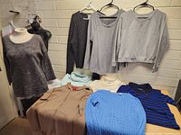 Wide view of lot of 10 sweaters and tops displayed on hangers and mannequins, showing various colors and styles