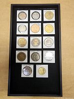 Top-down view of 14 commemorative coins and medallions arranged in a black display frame.